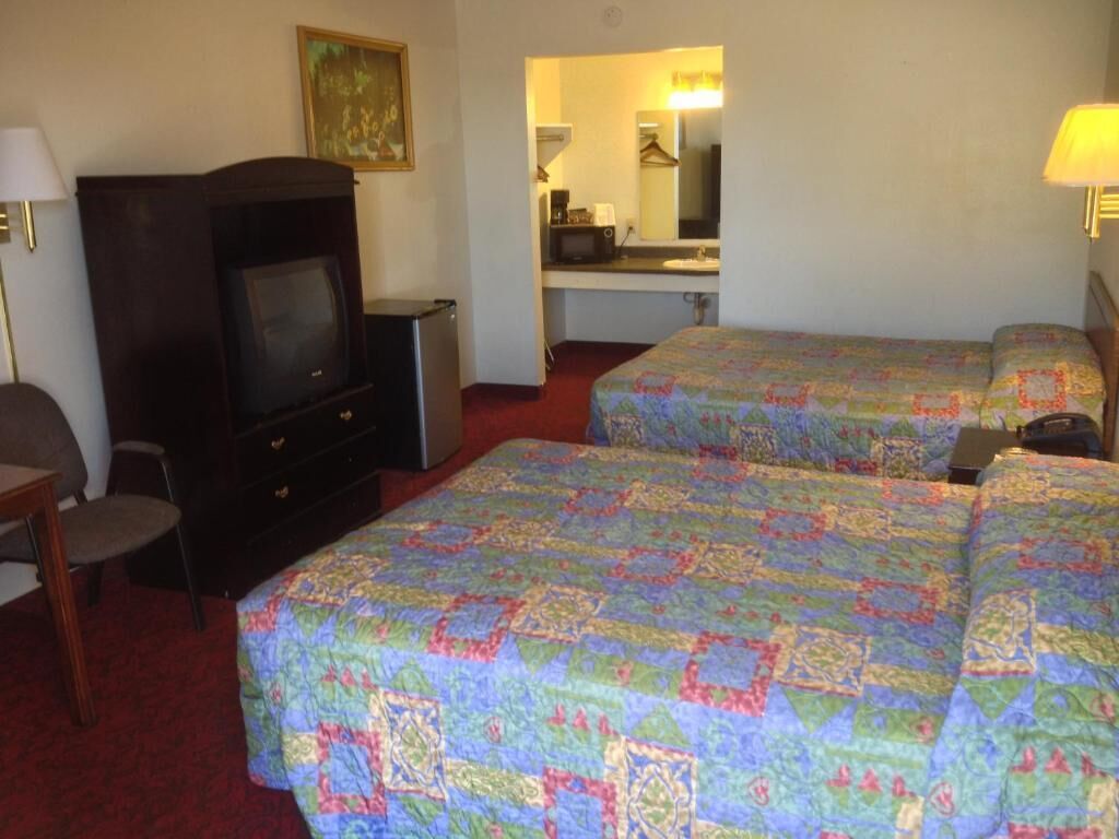 A hotel room with two beds, a TV, a desk, and a mirror.