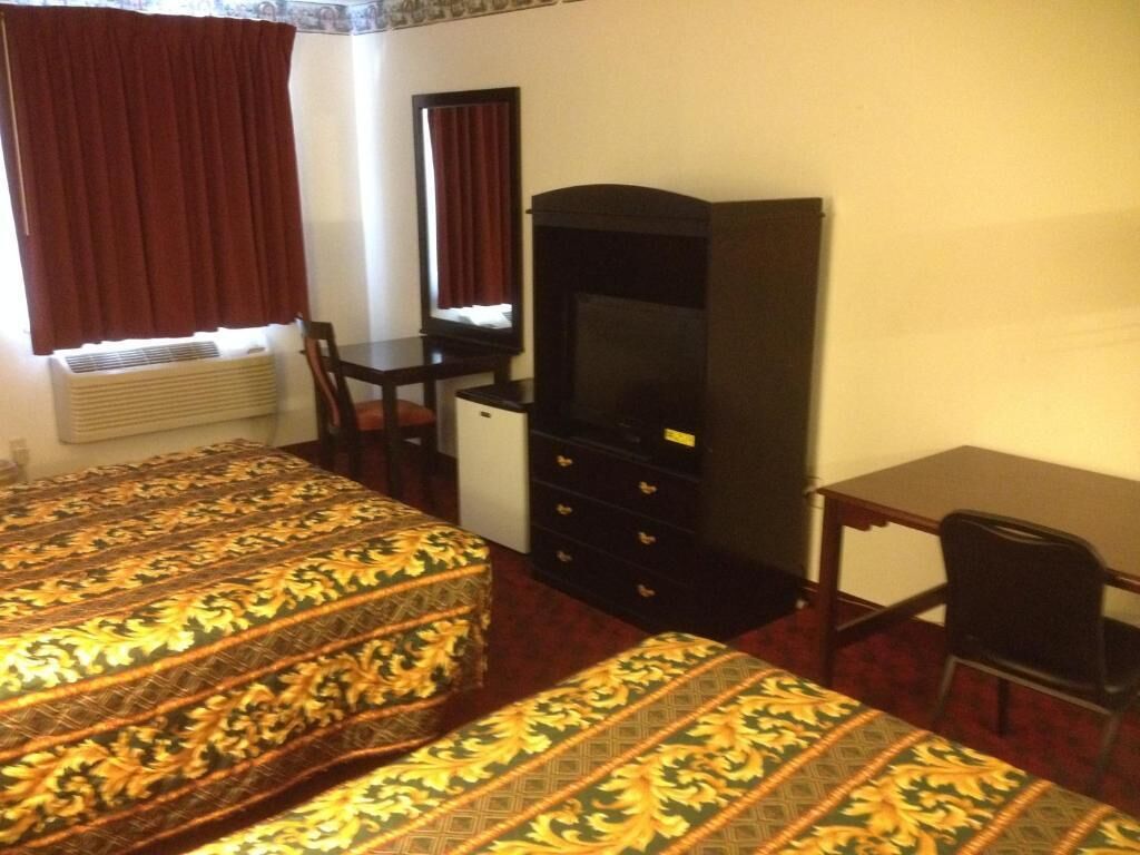 A hotel room with two beds, a desk, a dresser, and a television.