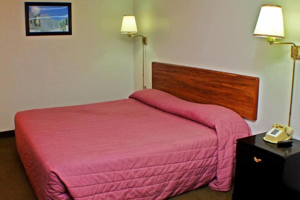 A hotel room with a bed, two bedside lamps, a nightstand with a phone, and a picture on the wall.