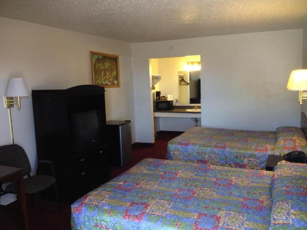 A hotel room with two beds, a TV, a desk, and a mirror.