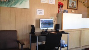 A reception desk with a computer monitor, a chair, and a small table. - American Dream (Elk City)