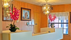 A reception desk with a wooden panel wall, a framed picture, and a chandelier. - American Dream (Elk City)