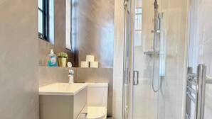 A modern bathroom with a glass shower enclosure, a toilet, and a sink with a mirror above it. - Sleek 1 Bedroom flat in Shoreditch, Old Street (London)