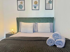 A neatly made bed with a green headboard, two pillows, and a rolled towel on the side. - Sleek 1 Bedroom flat in Shoreditch, Old Street (London)