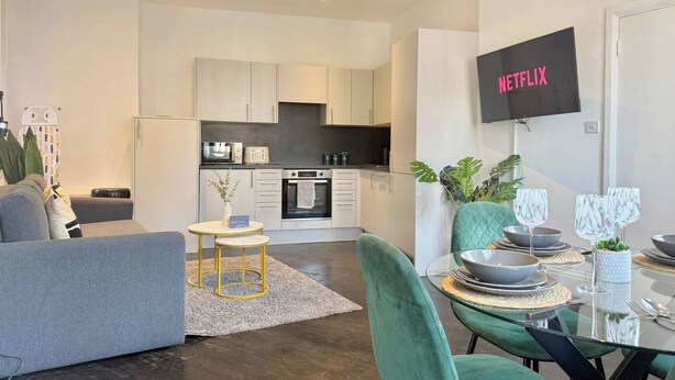 A modern living space with a dining area, kitchen, and a flat-screen TV mounted on the wall. - Sleek 1 Bedroom flat in Shoreditch, Old Street (London)
