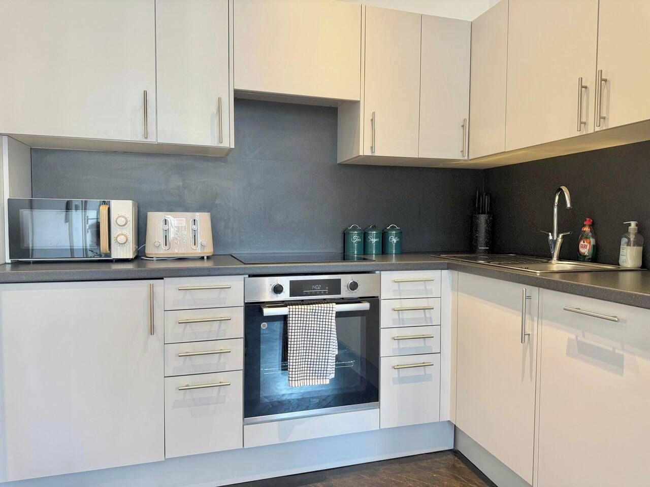 Een moderne keuken met witte kastjes, een ingebouwde oven, een magnetron en een broodrooster.