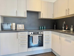 A modern kitchen with white cabinets, a built-in oven, a microwave, and a toaster. - Sleek 1 Bedroom flat in Shoreditch, Old Street (London)