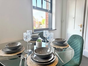 A dining table set with plates, bowls, and wine glasses, with a view of a building through a window. - Sleek 1 Bedroom flat in Shoreditch, Old Street (London)