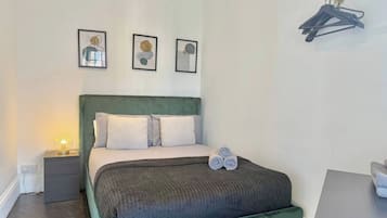 En pænt redt seng med grønt sengegavl, et natbord med lampe og et vægmonteret knagered.