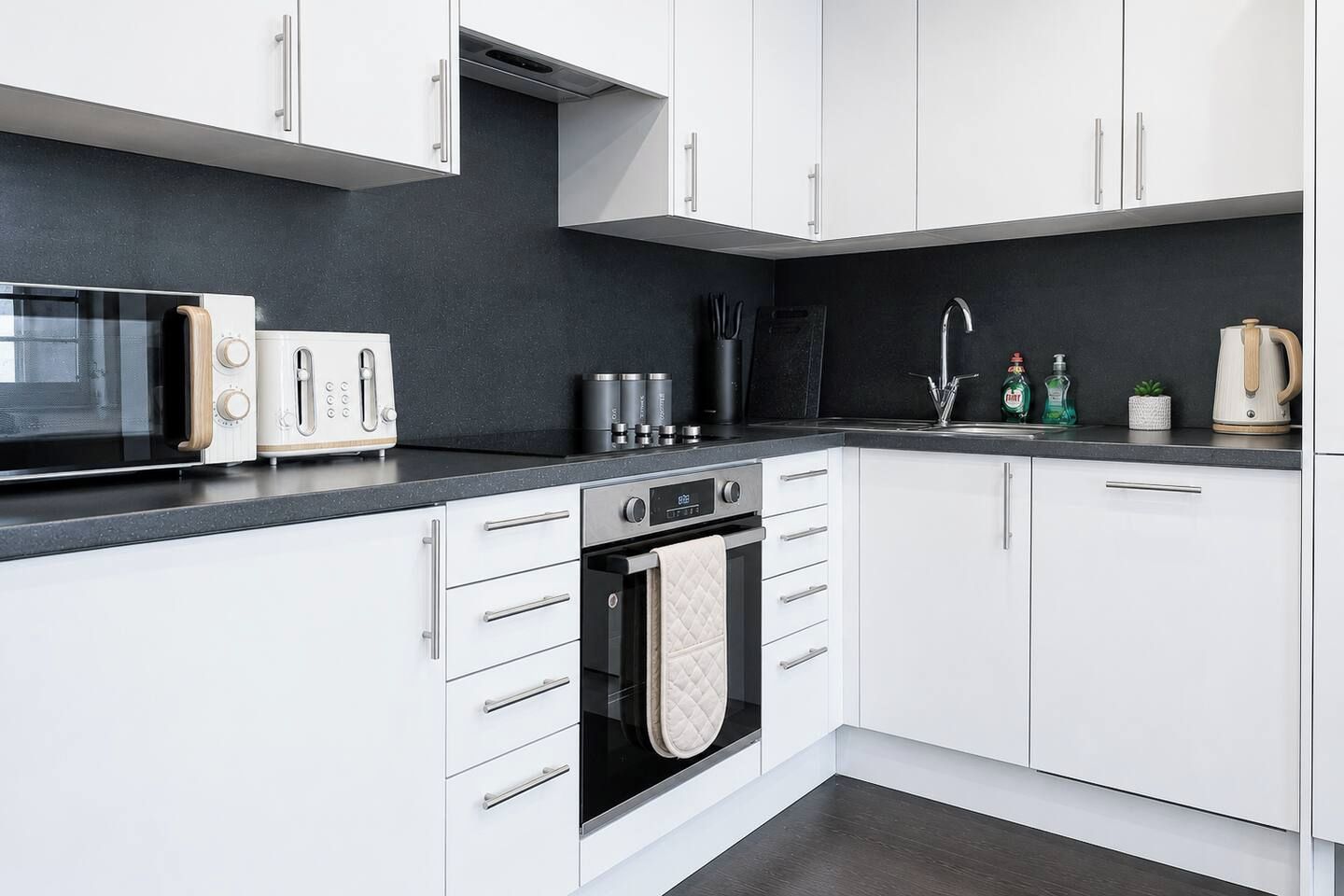A modern kitchen with white cabinets, a black countertop, a microwave, a toaster, a kettle, and a sink.