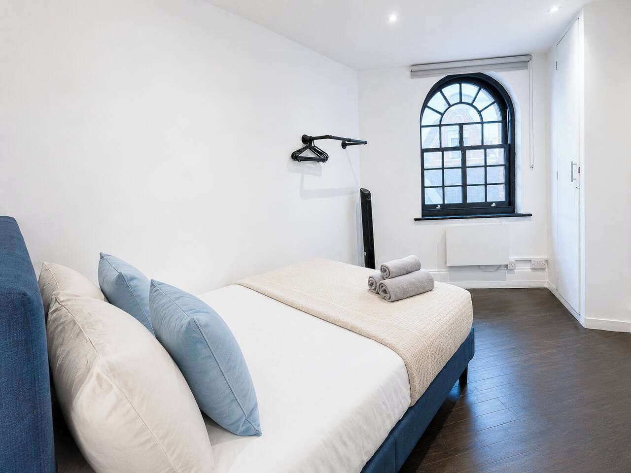 Een slaapkamer met een bed, een raam, een radiator en een kapstok.