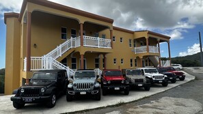 A row of SUVs parked in front of a yellow building with a balcony and stairs.