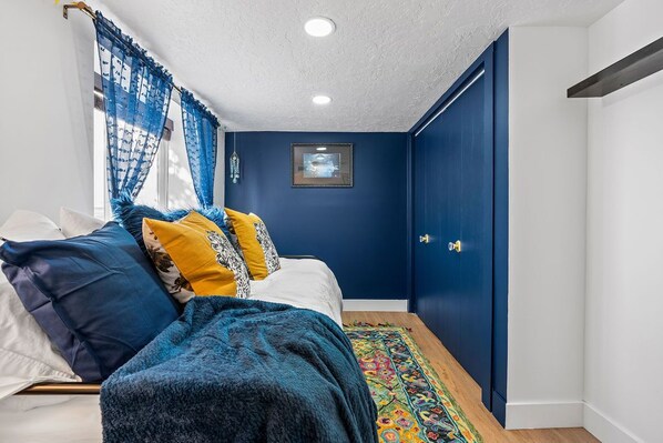 A bedroom with a bed, blue walls, a framed picture on the wall, and a door with a handle.