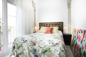 A bedroom with a bed, two bedside lamps, a window, and a colorful wall.