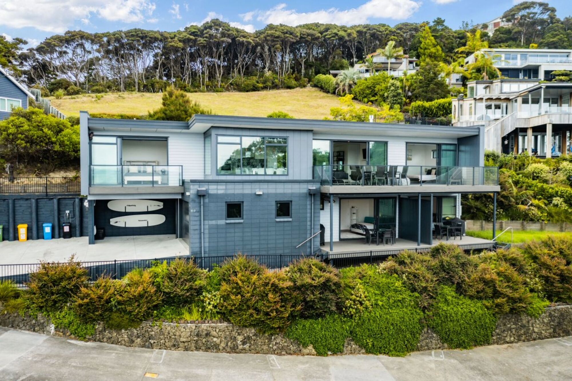 A modern two-story house with a balcony, a garage, and a stone retaining wall.