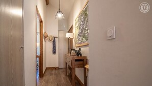 A narrow hallway with wooden flooring, a wooden bench, a wall-mounted lamp, and a framed picture on the wall. - Residence Mont- Blanc Lodge - LA Fleche (HAUTELUCE)