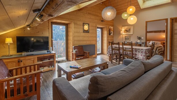 A cozy wooden cabin interior with a TV, sofa, dining table, and a balcony with a view. - Residence Mont- Blanc Lodge - LA Fleche (HAUTELUCE)