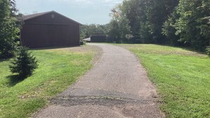 Een geplaveid pad dat naar een gebouw met een groen dak leidt, omgeven door gras en bomen.