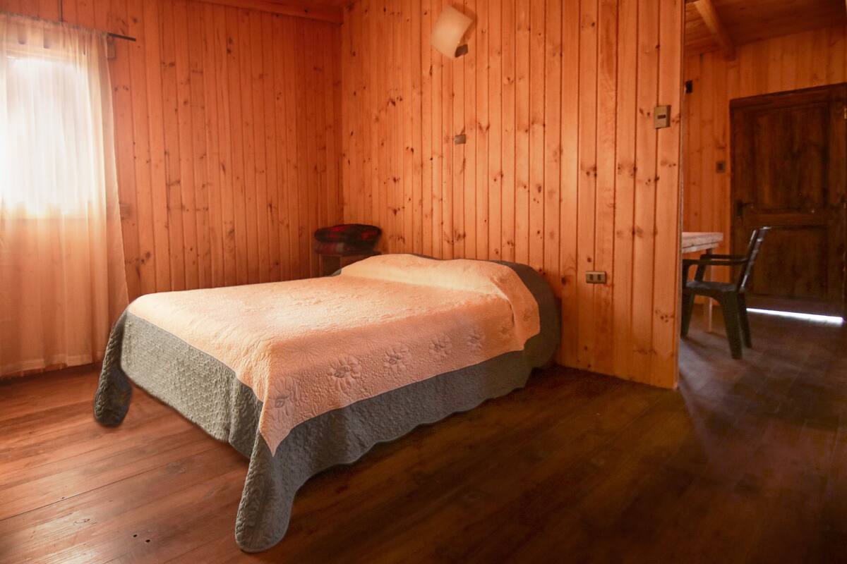 Een houten kamer met een bed, een stoel en een klein tafeltje.