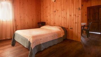 A wooden room with a bed, a chair, and a small table.
