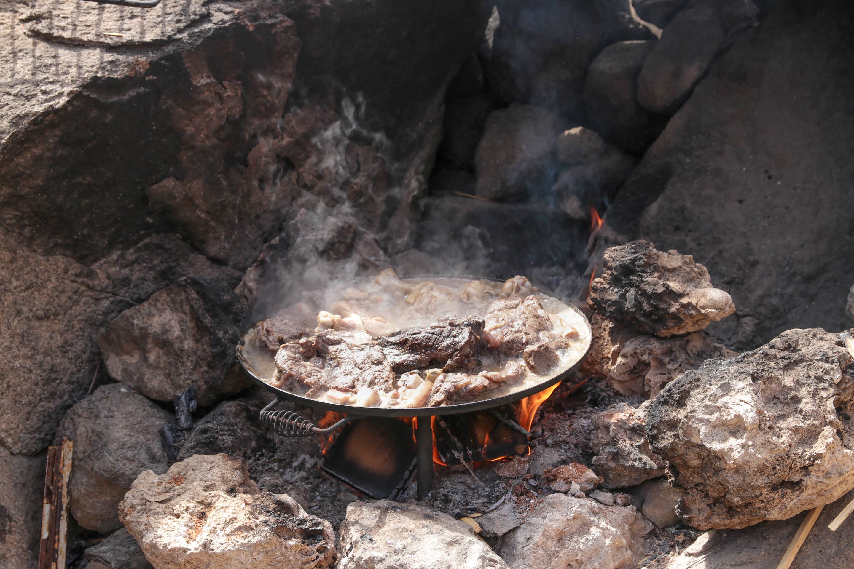 Una estufa portátil de cocina con una olla de metal sobre rocas, rodeada de llamas y humo.