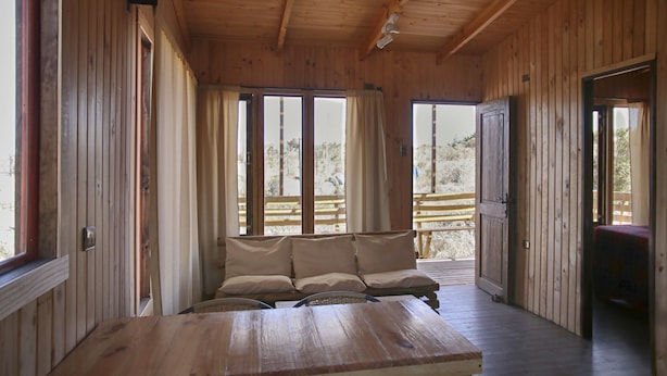 L’intérieur d’un chalet en bois, avec un canapé, de grandes fenêtres et une table en bois.