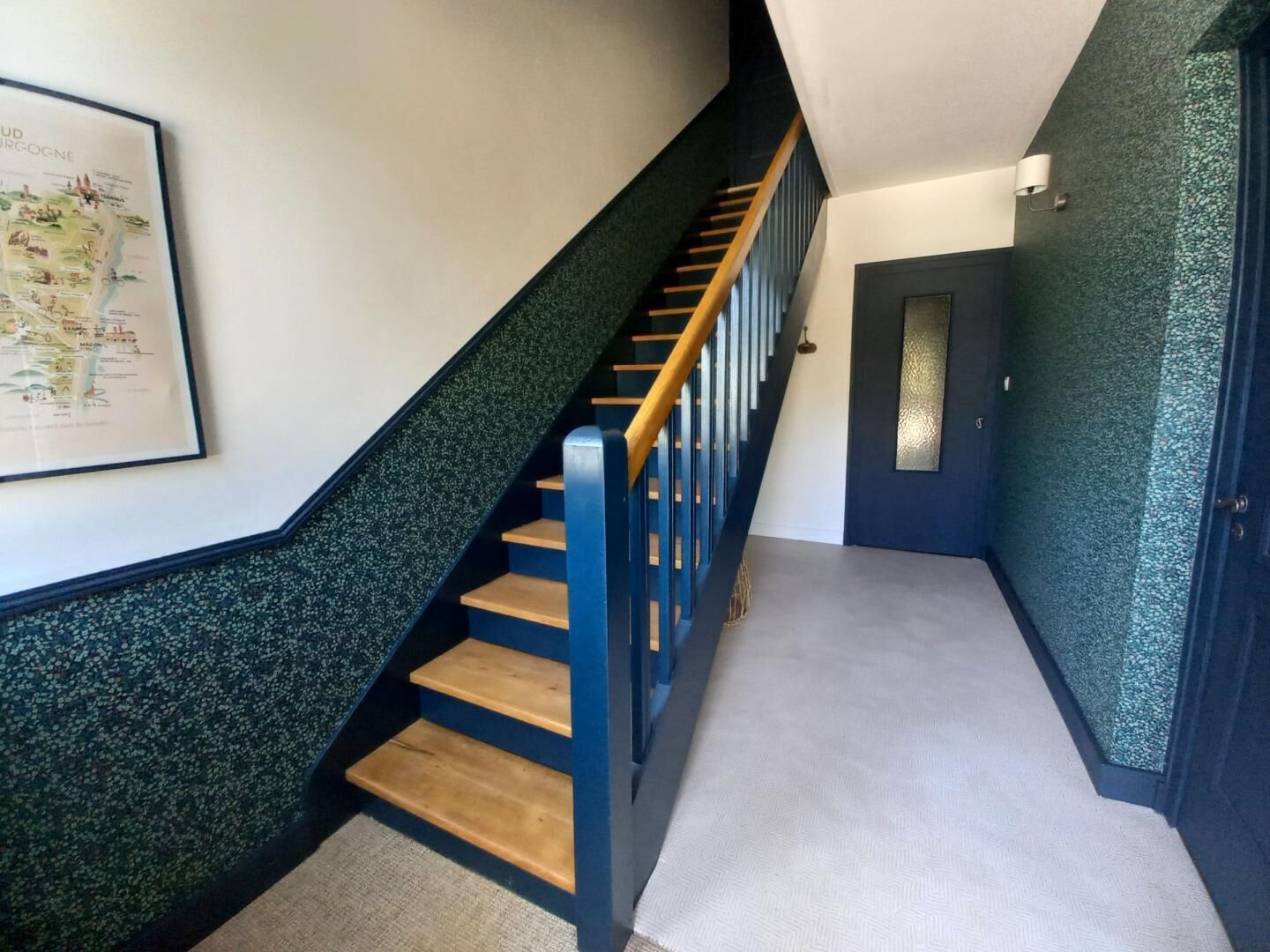 A staircase with wooden steps and blue handrails, leading to a door with a frosted glass panel.