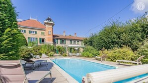 Ein Schwimmbecken mit Liegestühlen und einem Gebäude im Hintergrund.