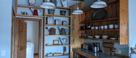 A kitchen with wooden shelves, hanging lights, and various kitchen utensils.