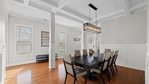 Un comedor con una mesa y sillas de madera oscura, paredes blancas y un colgante.