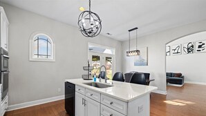Una cocina moderna con una isla central, armarios blancos y una lámpara colgante.
