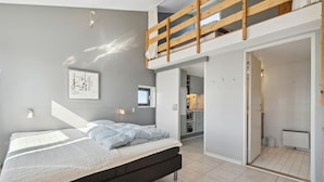 A modern bedroom with a loft bed, a small kitchenette, and a bathroom visible through an open door. - Awesome apartment in Fanø with WiFi (Fanø)