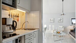 A modern kitchen with a built-in coffee maker, a sink, and a range hood. There is a dining area with a glass table and chairs, and a sofa. - Awesome apartment in Fanø with WiFi (Fanø)