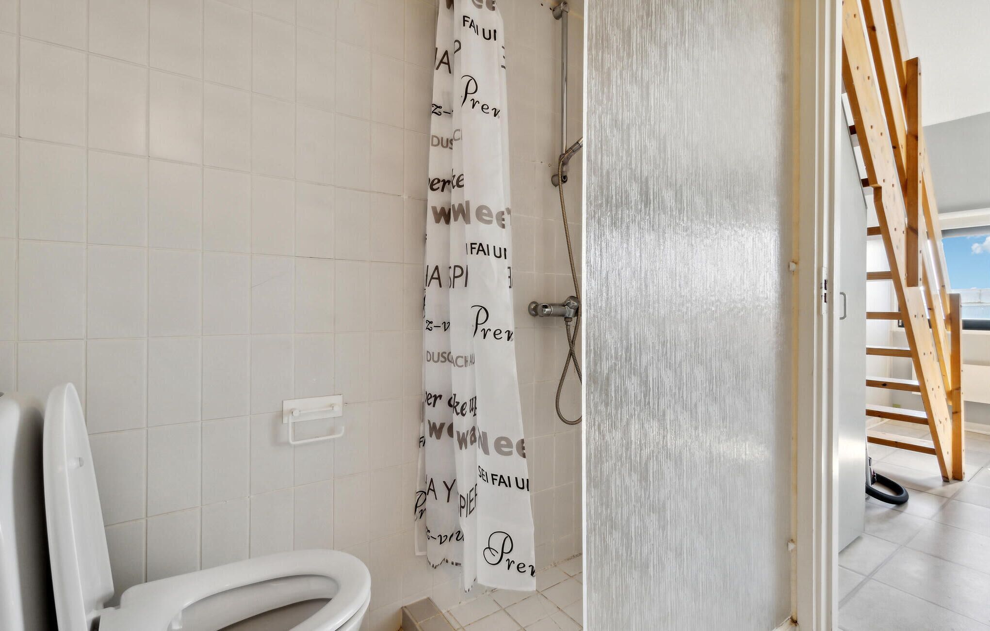 A bathroom with a toilet, a shower curtain with text, and a wooden ladder in the background.