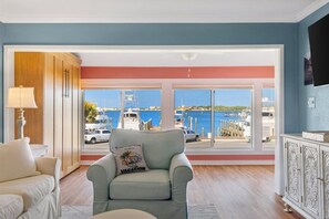 A room with a view of a marina, a sofa, a chair with a pillow, and a cabinet.