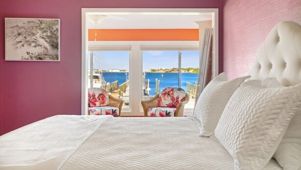 A bedroom with a large bed, a view of the sea, and wicker chairs by the window. - Amazing Marina Views | Baypoint Resort | Golf Course (Panama City Beach)