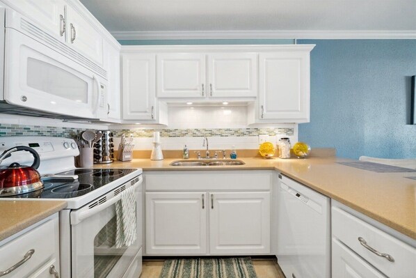 A kitchen with white cabinets, a microwave, stove, sink, and a tiled backsplash.