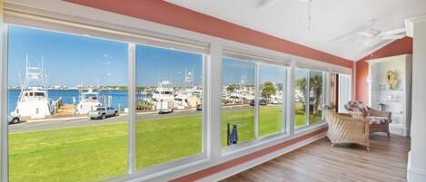 A room with large windows, a ceiling fan, and a view of a marina with boats.