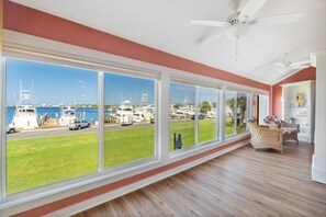A room with large windows, a ceiling fan, and a view of a marina with boats.