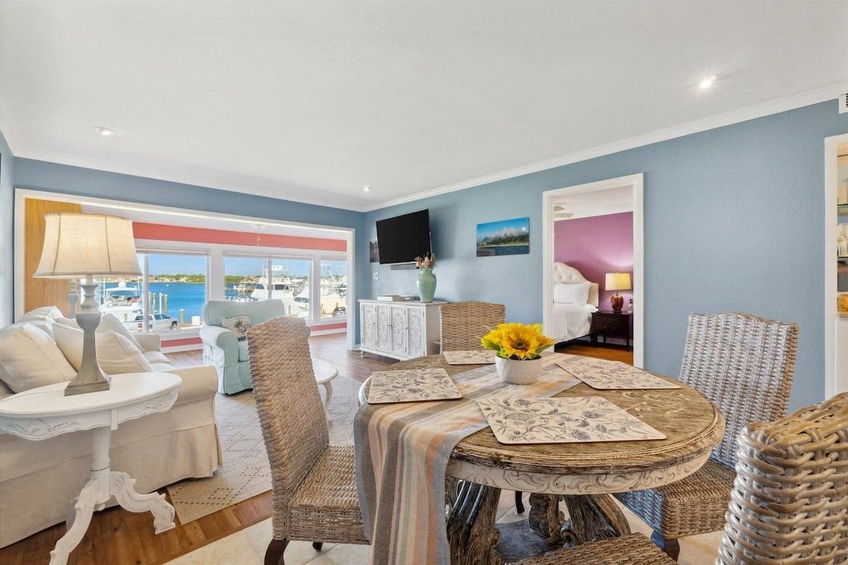 A dining area with wicker chairs, a round table, and a view of the outside.
