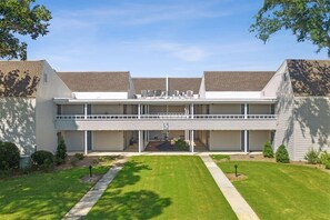 A two-story building with a flat roof, a covered parking area, and a well-maintained lawn.