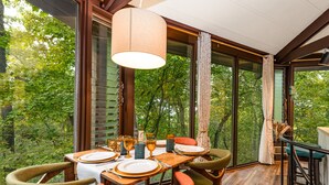 Un comedor con una mesa dispuesta para cuatro personas, rodeado de ventanas amplias que ofrecen vistas al bosque.