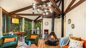 Una sala de estar acogedora con chimenea, muebles de madera y grandes ventanales que ofrecen vistas al exterior.