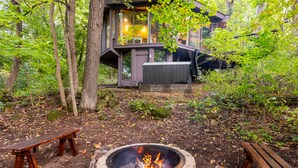Une cabane avec un foyer entouré d’arbres, un banc et un jacuzzi.