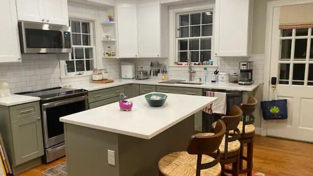 A kitchen with white cabinets, a central island, and a dining area with bar stools.