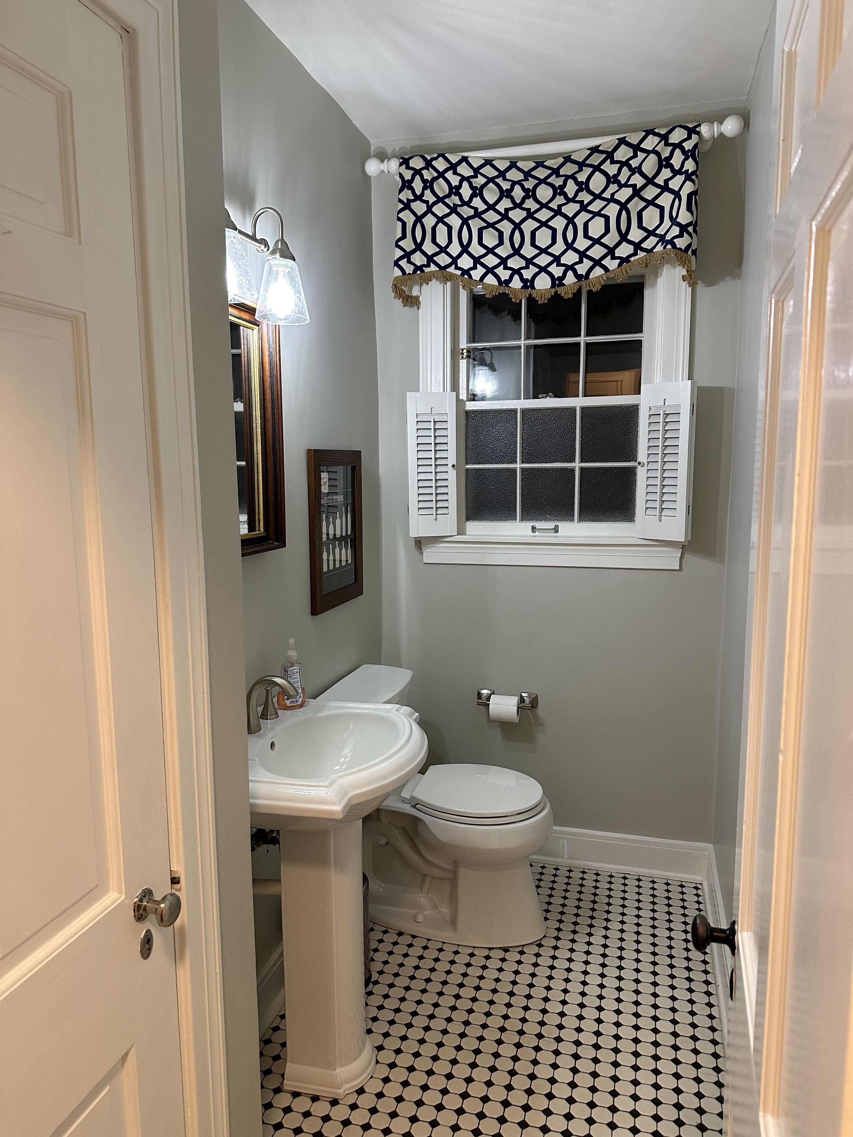 A bathroom with a white sink, toilet, and window with shutters.