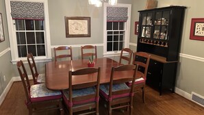 A dining room with a wooden table, six chairs, a chandelier, and a black cabinet with glass doors.