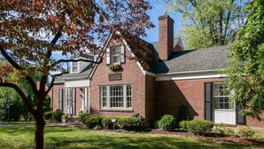 A two-story brick house with a gabled roof, a front porch, and a well-maintained lawn.