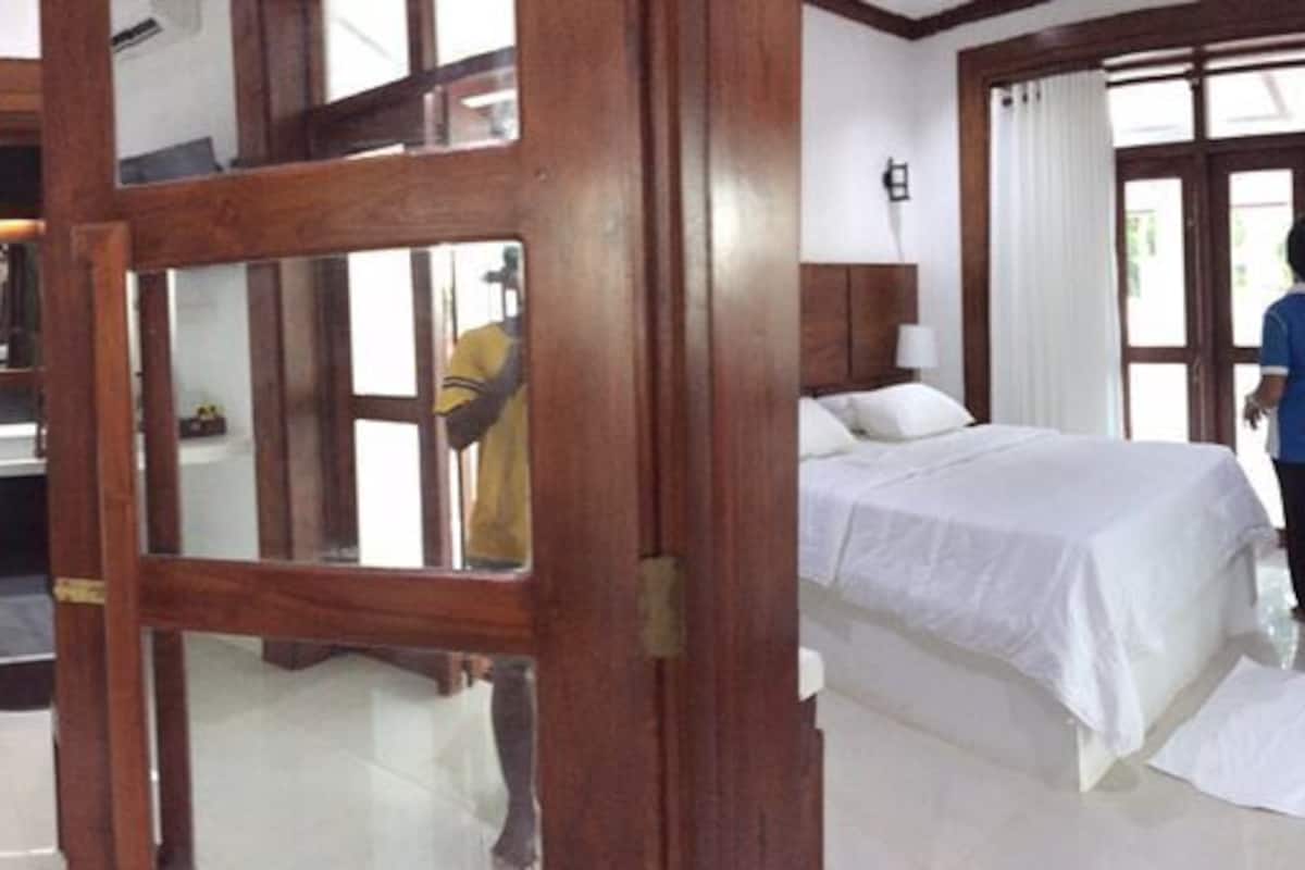 A hotel room with a bed, a desk, a chair, a mirror, and a window with curtains.
