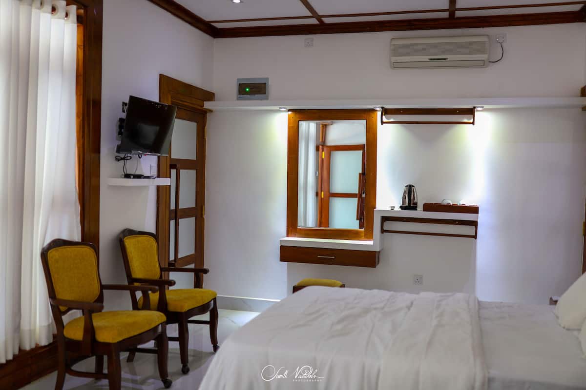 A hotel room with a bed, a TV mounted on the wall, a window with a wooden frame, and a desk with a mirror.
